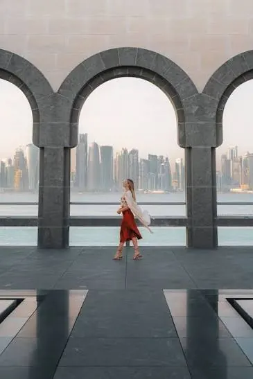Visitor walking beneath stone arches overlooking the water and Doha skyline