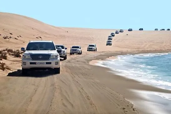 White 4x4 SUV convoy on golden dunes beside the Inland Sea at Khor Al Adaid, Qatar