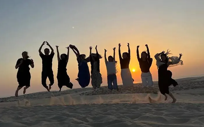 Guests jumping on sand dunes at sunset during a Qatar desert safari