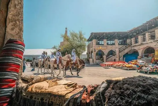 Camel riders passing traditional market stalls with colourful textiles in Qatar