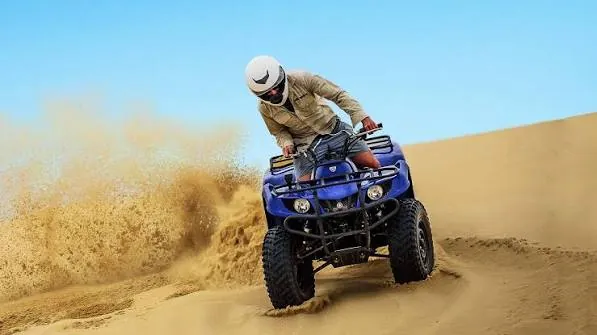 Blue quad bike ATV riding over red sand dunes on a Doha desert adventure