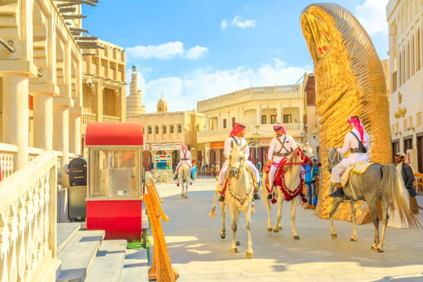 Doha, Qatar - February 20, 2019: police officers, famous attraction, riding white Arabian horses at Souq Waqif. Fanar Islamic Cultural Center with Mosque and golden giant thumb sculpture on background